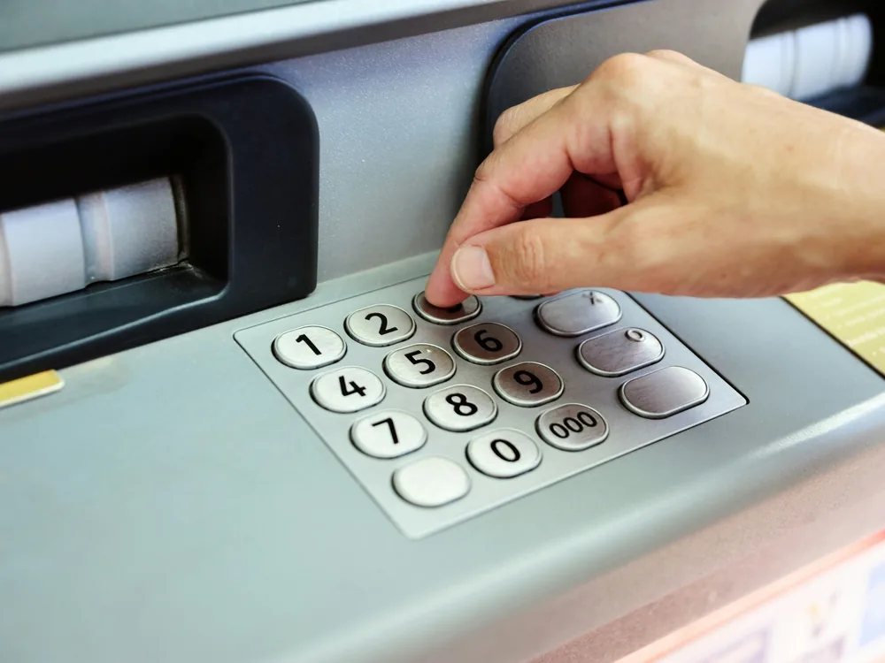 Persona ingresando su clave en el teclado de un cajero automático, enlace al servicio de fraude bancario de Indemnia